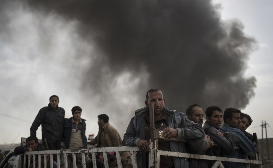 Displaced people stand on the back of a truck Tuesday at a checkpoint near Qayara, south of Mosul, Iraq,