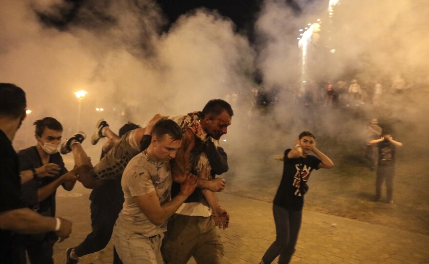 Protesters carry a wounded man during clashes with police early Monday in Minsk after the presidential election.