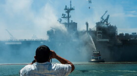A man watches as an MH-60S Seahawk helicopter from the “Merlins” of Helicopter Sea Combat Squadron 3 provides aerial firefighting support in the firefight aboard amphibious assault ship USS Bonhomme Richard on July 13, 2020.