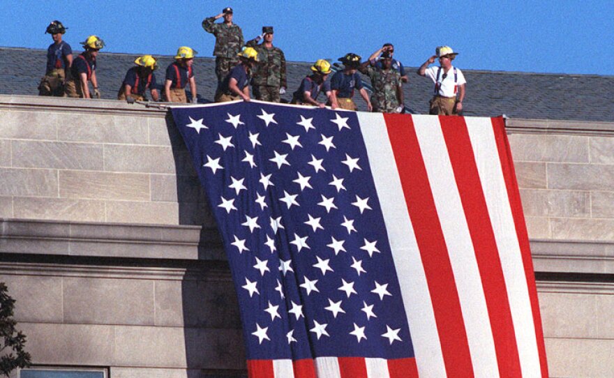 Fire fighters and military personal on the roof of the Pentagon unfurl a large American flag, Arlington County, Va., Sept. 12, 2001.