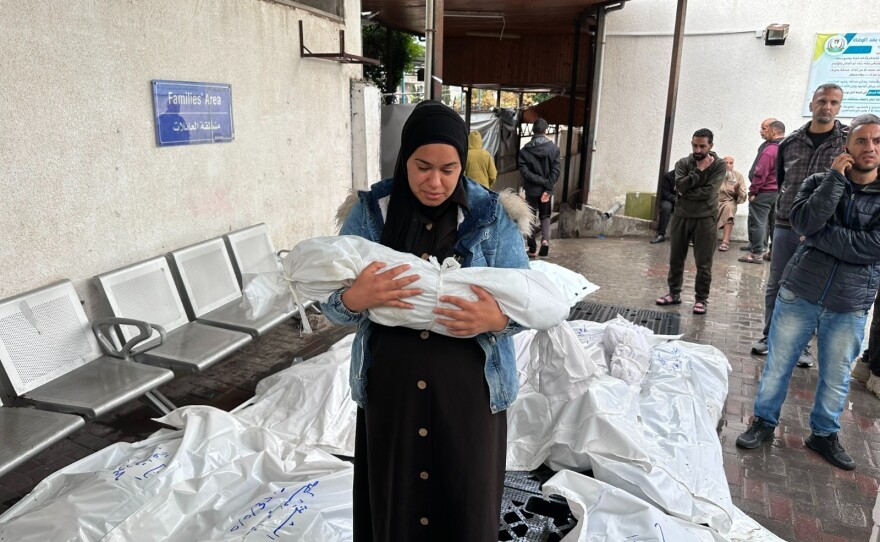 A woman carries a child in a white shroud in front of a "Families Area" sign next to the bodies of others killed in an Israeli airstrike on a home in Rafah on May 6, 2024.