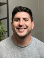 Man in grey shirt with dark hair smiling.
