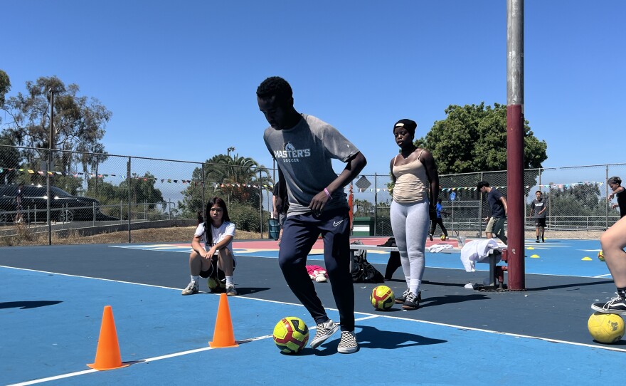 Mbekalo Oredi demonstrates how to dribble a soccer ball to a group of young girls at Colina Del Sol Park, July 10, 2025.