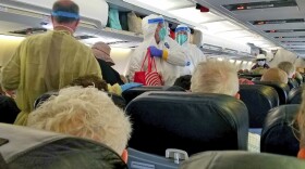 This photo by Michele Smith shows crewmembers in protective garb helping Grand Princess cruise ship passengers get settled aboard a plane that will take them to Marine Corps Air Station Miramar for further quarantine after leaving the ship in Oakland, Calif., Wednesday, March 11, 2020. 