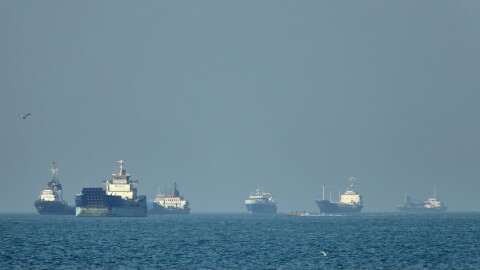Cargo ships, including bulk carriers and general cargo vessels, sit at anchor offshore as a small motorboat passes in the foreground, in the Strait of Hormuz off Bandar Abbas, Iran, Monday, May 4 , 2026.