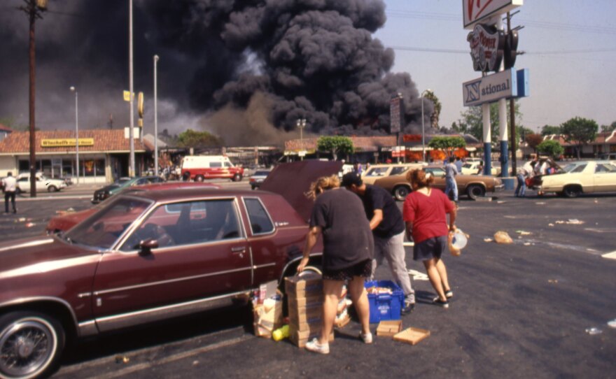 Looters load up a car at the Viva shopping center near a billowing fire during the rioting that erupted in Los Angeles on April 29, 1992, after a jury found four Los Angeles Police Department officers not guilty in the beating of Rodney King.