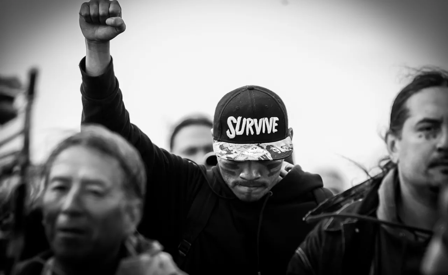 "Defending the Fire" poster. A man in the center wears a cap that reads "Survive."