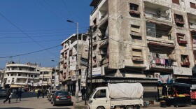 The city center of Jableh is home to older buildings as well as newer, less regulated construction. An image of President Bashar Assad hangs over a street cart with the slogan "We continue with you" in Arabic.