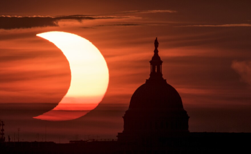 In this photo provided by NASA, a partial solar eclipse is seen as the sun rises to the left of the U.S. Capitol in Washington, Thursday, June 10, 2021, as seen from Arlington, Va.