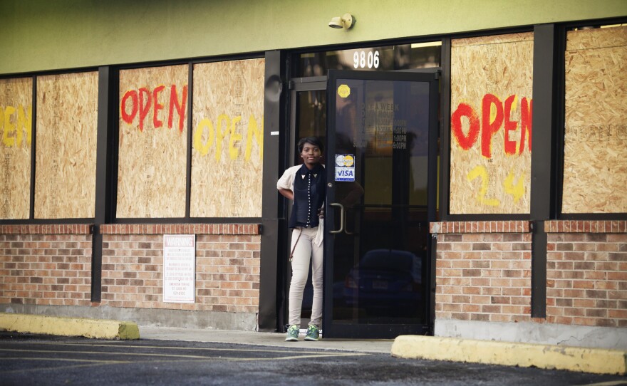 A woman stands before a restaurant on West Florissant Avenue where rioting took place earlier this week. Most of the stores on this stretch are boarded up — some after they were damaged by looters, and some as a precaution — even as many remain open for business.