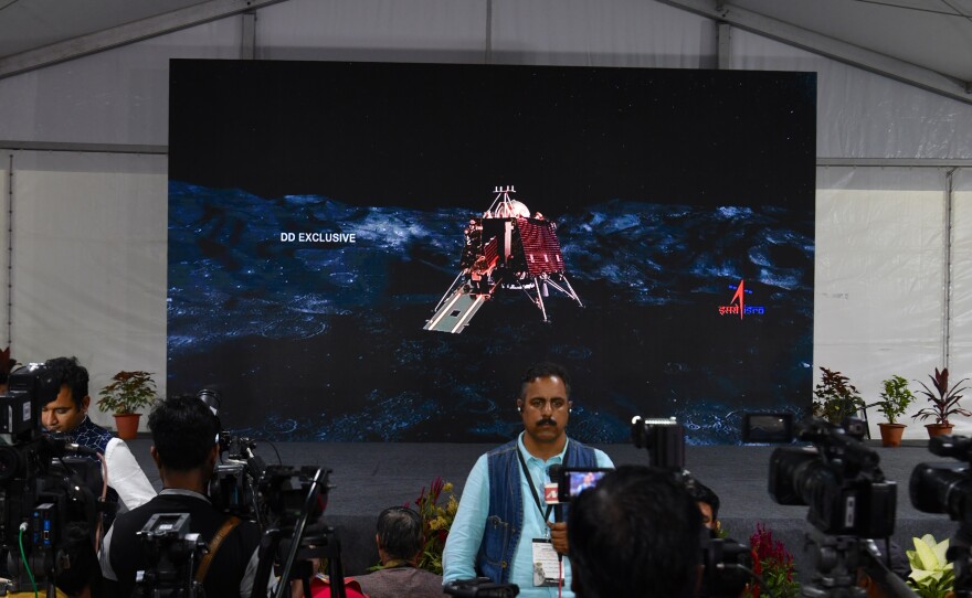 An illustration of the landing craft stands behind members of the media at an Indian Space Research Organisation facility this year in Bangalore, India. Authorities initially chalked up the failed landing in September to a loss of communication with the craft; last week, they revealed what happened to it.