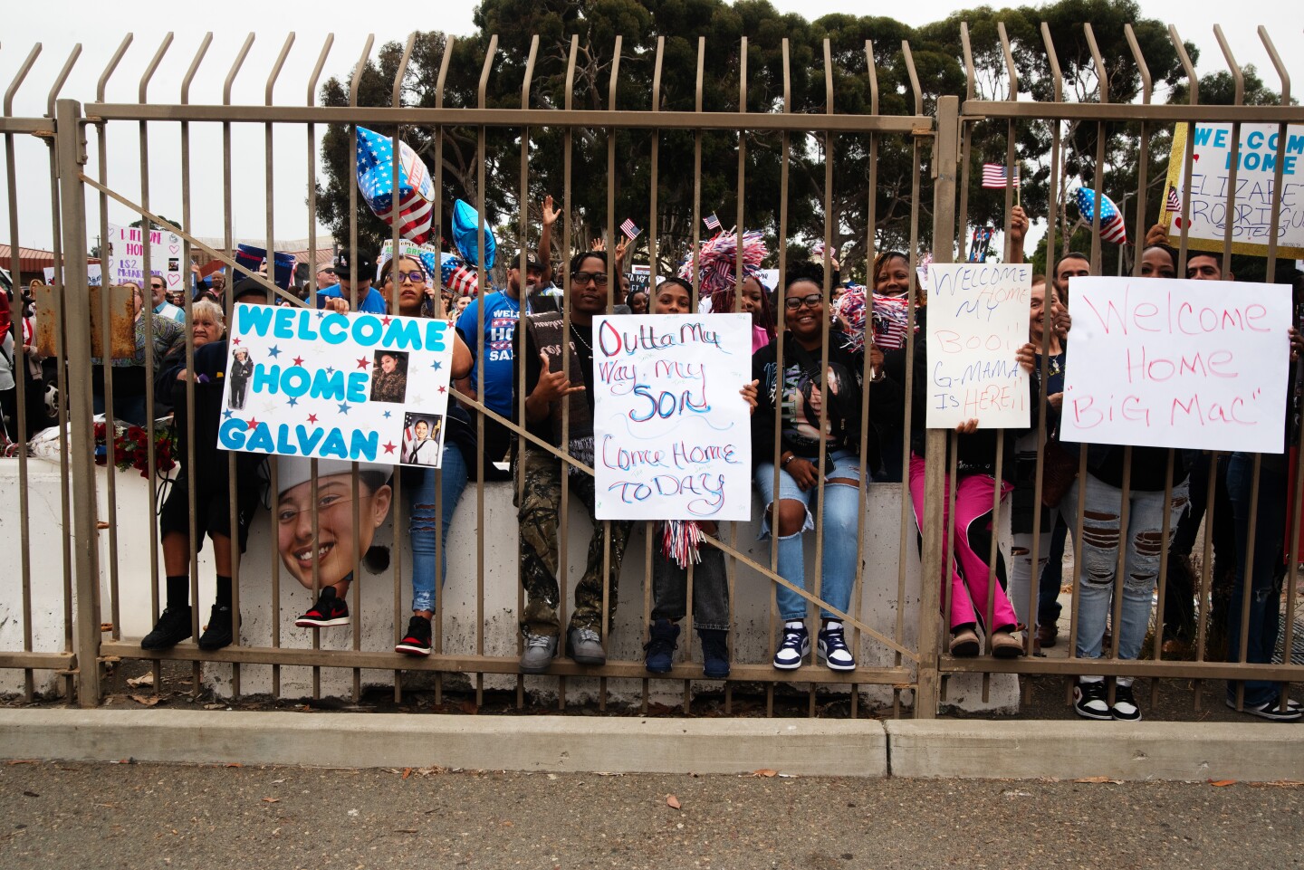 Families wait for their loved ones hold signs through the fence keeping them off the dock Aircraft carrier Theodore Roosevelt prepares to unload on Oct 15, 2024 at the Naval Air Station North Island on Coronado Island.