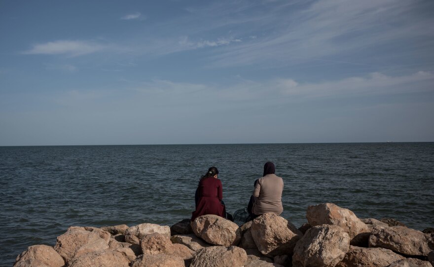 People sit by the seaside looking north towards the Mediterranean Sea, in the town of Sfax.