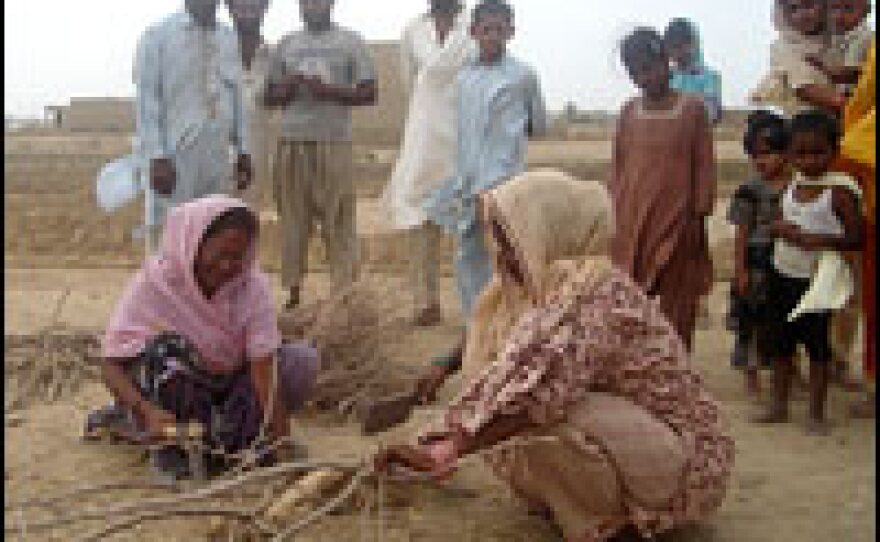 Two women chop wood for fuel just outside their homes in the desert on the outskirts of Karachi.
