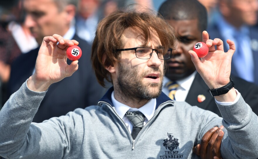 Comedian Lee Nelson is taken away by security Friday while holding golf balls stamped with swastikas, as he protests Donald Trump, at the opening of Trump's resort in Scotland.