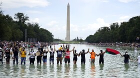 In this Friday, Aug. 28, 2020, file photo, people join hands as they pose for a photo in the Reflecting Pool in the shadow of the Washington Monument as they attend the March on Washington, at the Lincoln Memorial in Washington, on the 57th anniversary of the Rev. Martin Luther King Jr.'s "I Have A Dream" speech. 