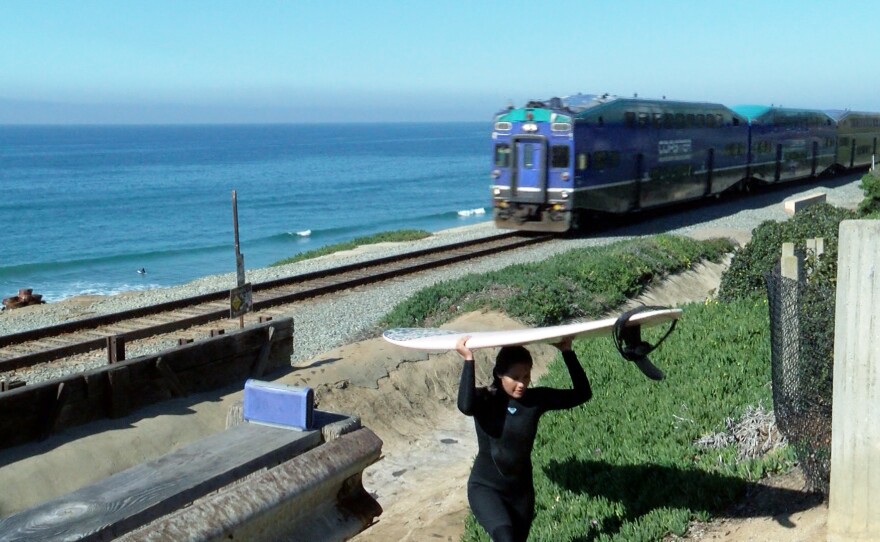 A surfer going back up the bluff in Del Mar as a Coaster train passes behind her on Jan. 21, 2022.