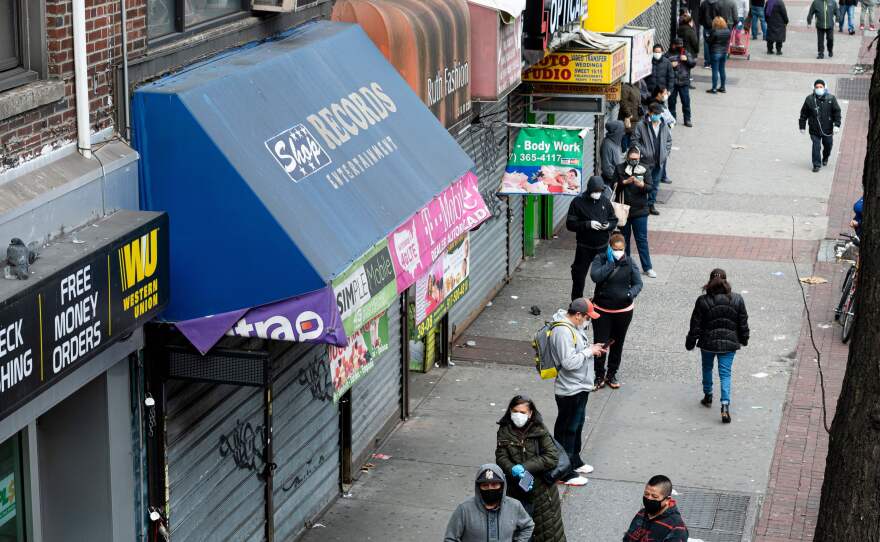In the Queens borough of New York City on Tuesday, people wearing face masks wait in line to enter a store that offers check-cashing services.