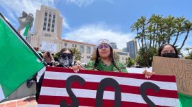 Karina Avila (center) holds an upside down American flag with the letters "SOS" on it at the "No Kings" Day protest in downtown San Diego on June 14, 2025. "No Kings" Day is part of a nationwide demonstration against the policies of the Trump administration. 