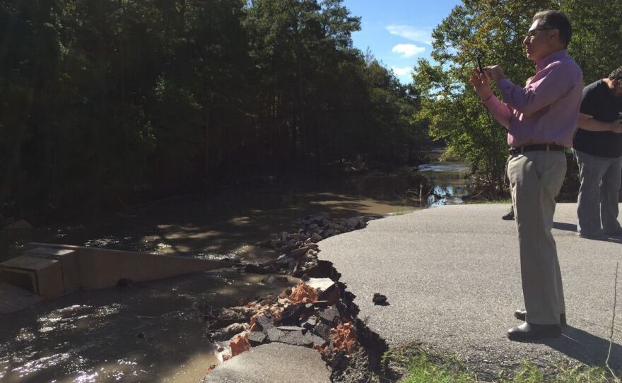 People survey the Carys Lake dam and bridge in Columbia, S.C., Tuesday. The dam was washed away after surging waters swept through the area. Further downstream, Forest Lake overspilled its dam and flooded other parts of the Columbia suburbs.