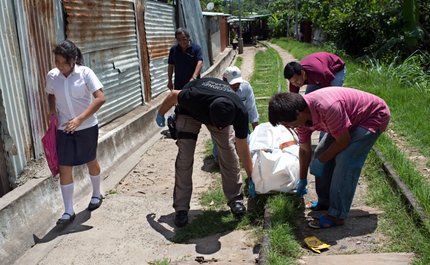 A girl looks away from the body of an assassinated man, who was killed by a gang member in San Salvador.