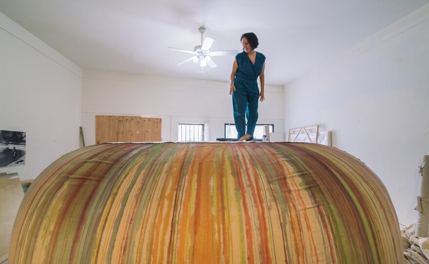 Artist Carmen Argote stands atop the in-progress sculpture for "Filtration System," a large mound covered in colorfully-streaked cloth.