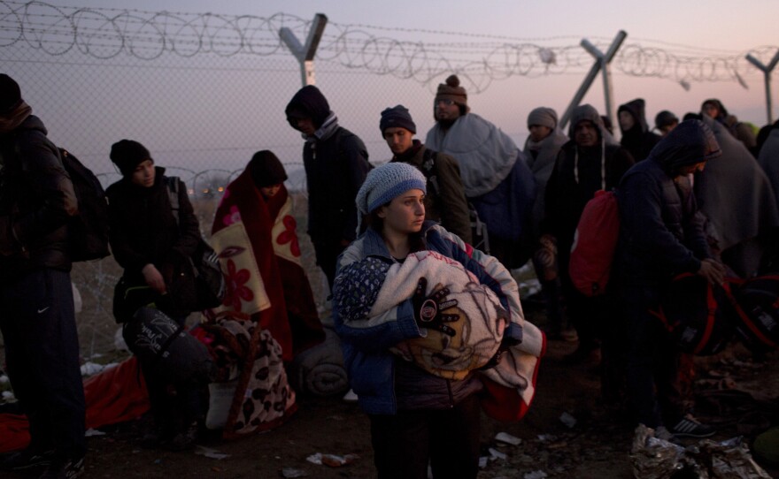 A woman holds her baby as she waits with other migrants on the Greek side of the fence along the border with Macedonia on Sunday. Macedonian is only allowing in refugees from the war-torn countries of Syria, Iraq and Afghanistan. Those not allowed into Macedonia are being bused to a sports stadium in Athens.