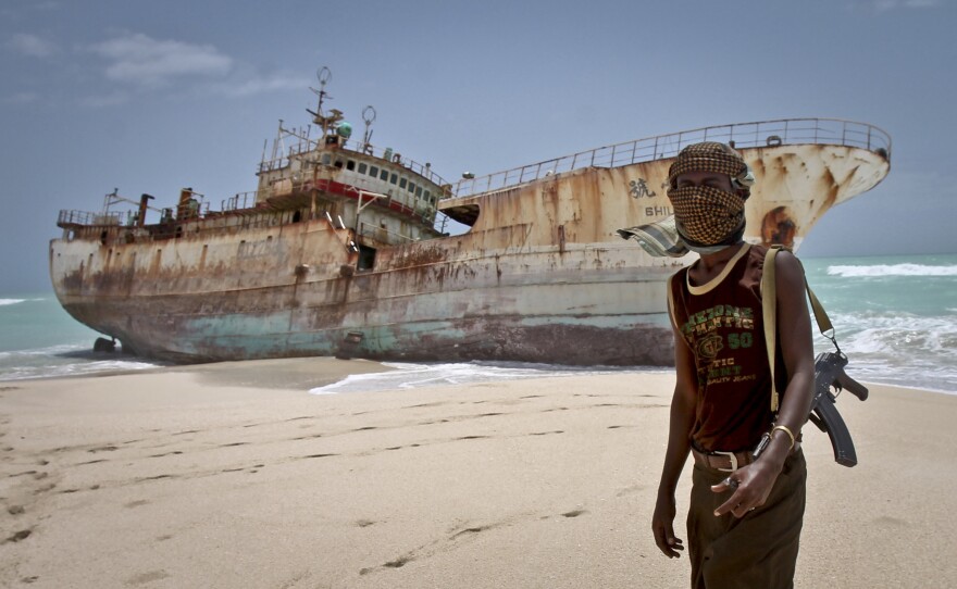 A masked Somali pirate stands near a Taiwanese fishing vessel that washed up in 2012 after the pirates were paid a ransom and released the crew. The image appears on the cover of Michael Scott Moore's new book <em>The Desert and the Sea.</em>