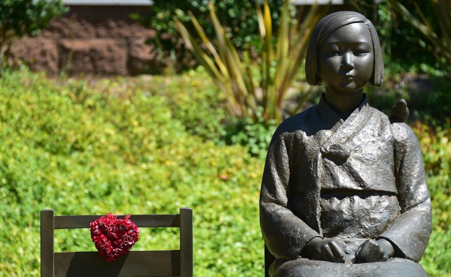 The Comfort Woman statue, with bird on shoulder, beside an empty chair symbolizing survivors who are of an old age without having yet witnessed judgement, in Glendale, California.