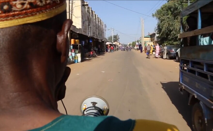 A town crier rides his moped through the city of Kayes in Mali, using his megaphone to warn people about Ebola.