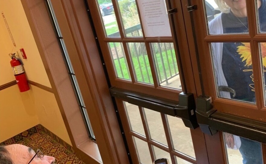 Luann Thibodeau visits her husband at his nursing home, with a glass door between them.