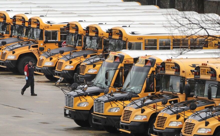 A worker passes public school buses parked at a depot in Manchester, N.H., last month. The state's public school buildings are closed to students through the end of the academic year.