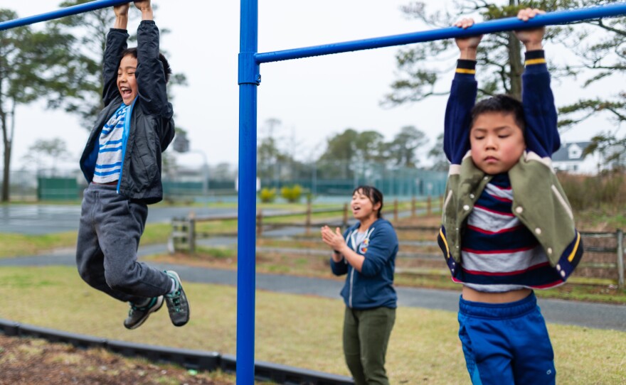 Thu Pham, center, encourages Henry, left, and Hayle, as they climb pull-up bars at a park on Chinqoteague Island, Md., on April 14, 2019.