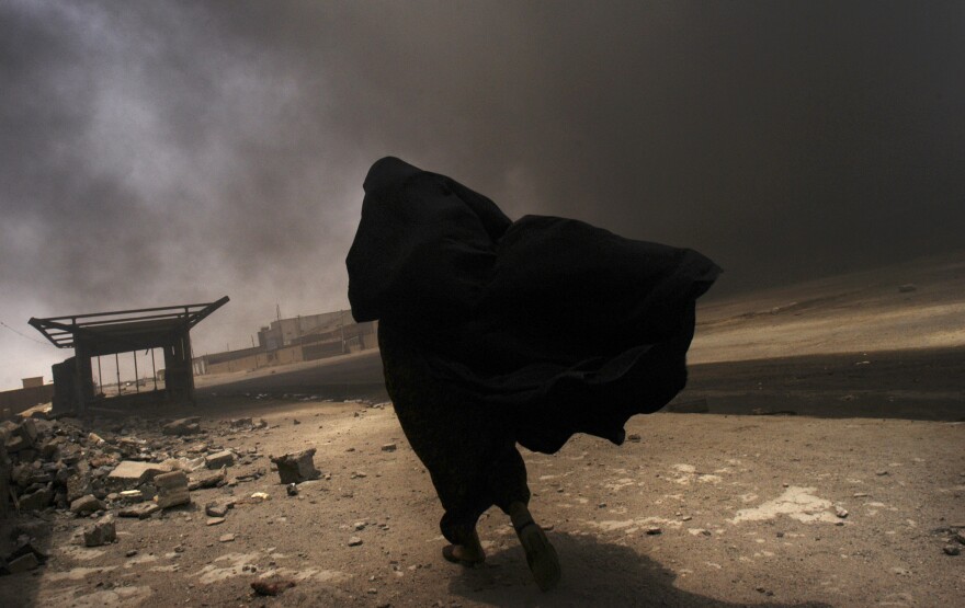 An Iraqi woman walks through a plume of smoke rising from a massive fire at a liquid gas factory as she searches for her husband in the vicinity in Basra, Iraq, May 2, 2003.