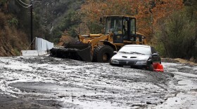 A bulldozer operator begins to clear a car trapped in a deep debris flow that covered parts of Topanga Canyon Boulevard near the village of Topanga west of Los Angeles, Tuesday, Jan. 9, 2017.