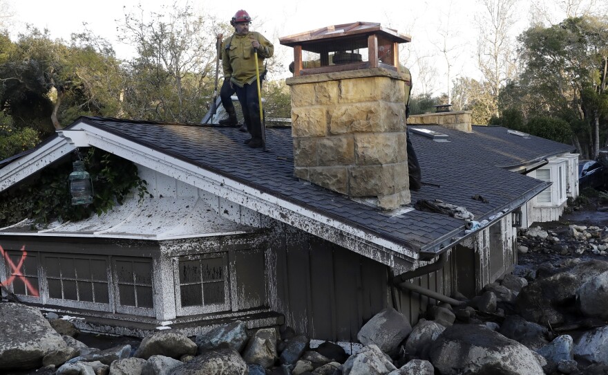 A firefighter stands on the roof of a house submerged in mud and rocks, Jan. 10, 2018, in Montecito, Calif.