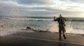 A man jumps back as waves hit rip rap, loose rocks that form a barrier, on The Strand in Oceanside, July 29,2015.