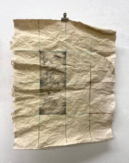Handmade paper with a grid of rectangles lined with copper and copper patina, with two rectangles colored in with graphite, is clipped to the wall.