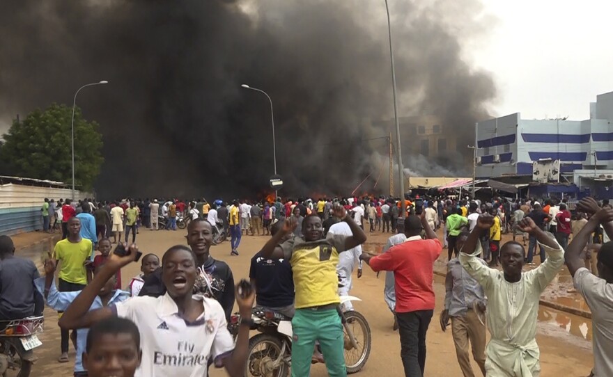 With the headquarters of the ruling party burning in the back, supporters of Niger's ruling junta demonstrate in Niamey, Niger, on July 27, 2023.