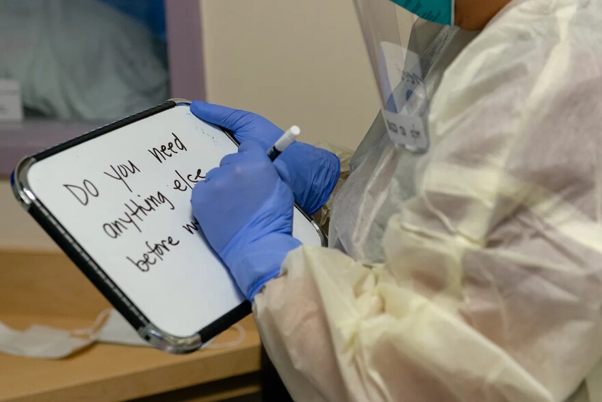 In June 2020, an ICU staffers is photographed communicating with one another health care worker through the windows using a whiteboard.