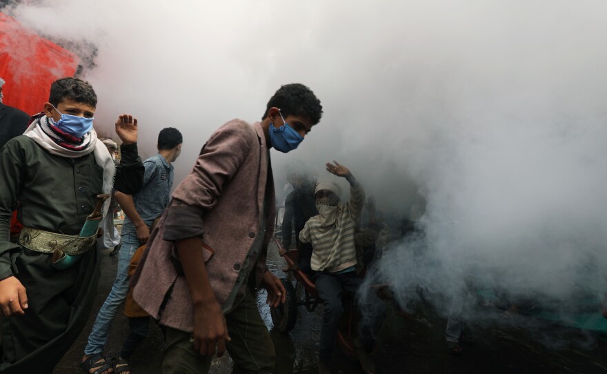 People wear face masks as health workers fumigate a market amid concerns about the spread of COVID-19 in Sanaa, Yemen.