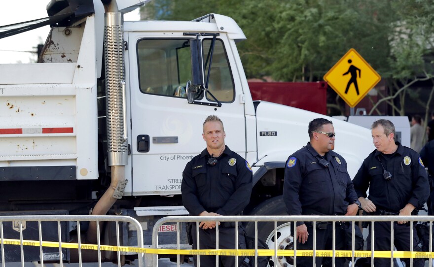Phoenix police officers stand beside a dump truck blocking a road outside the Phoenix Convention Center on Aug. 22. Protests were held against President Trump as he planned to host a rally inside the convention center.