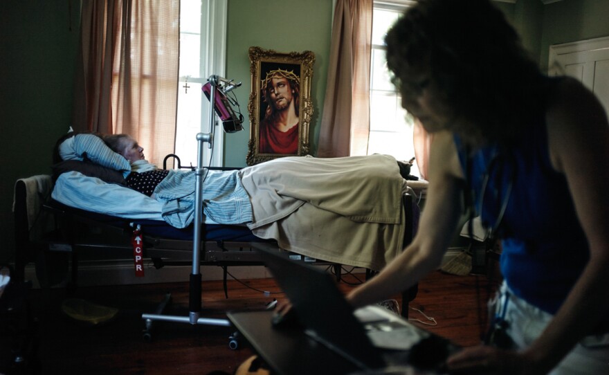 Patricia Gillihan, 71, lies in her home hospital bed while Miller checks her medical records.