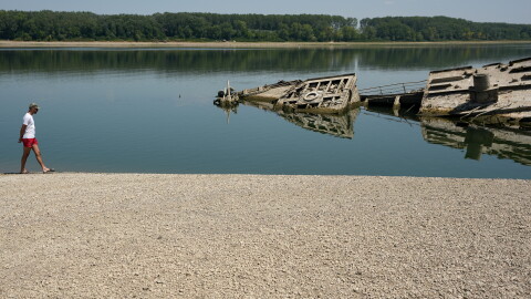 A man walks on a sandbank by the wreckage of a WWII German warship, which emerged during the drought in front of Djerdap II, a large dam on the Danube River between Romania and Serbia near Prahovo on Aug. 4, 2026.