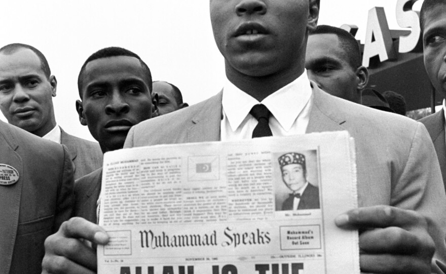 In this Nov. 22, 1965 file photo, heavyweight champion Muhammad Ali holds a "Muhammad Speaks" newspaper bearing his picture as he and followers of the Nation of Islam leave the Las Vegas convention center after weigh-in ceremonies to defend his title against challenger Floyd Patterson.