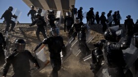 Mexican police run as they try to keep migrants from getting past the Chaparral border crossing in Tijuana, Mexico, Sunday, Nov. 25, 2018, near San Ysidro, California. 
