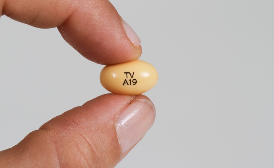 A progesterone pill held between a woman's fingers.