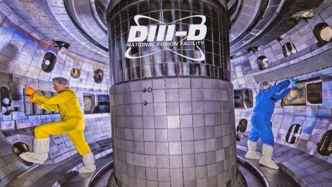 Two scientists, one wearing yellow coveralls and the other wearing blue coveralls, complete work on th DIII-D tokamak nuclear fusion reactor, operated by General Atomics in San Diego.