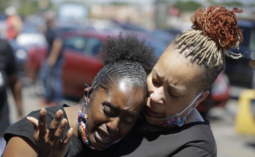 Two women pray in Louisville, Ky., in early June near the intersection where David McAtee was killed. Louisville police say video obtained from security cameras at McAtee's barbecue restaurant and an adjoining business show that McAtee fired a gun as police and National Guard soldiers were enforcing a curfew approached his business.