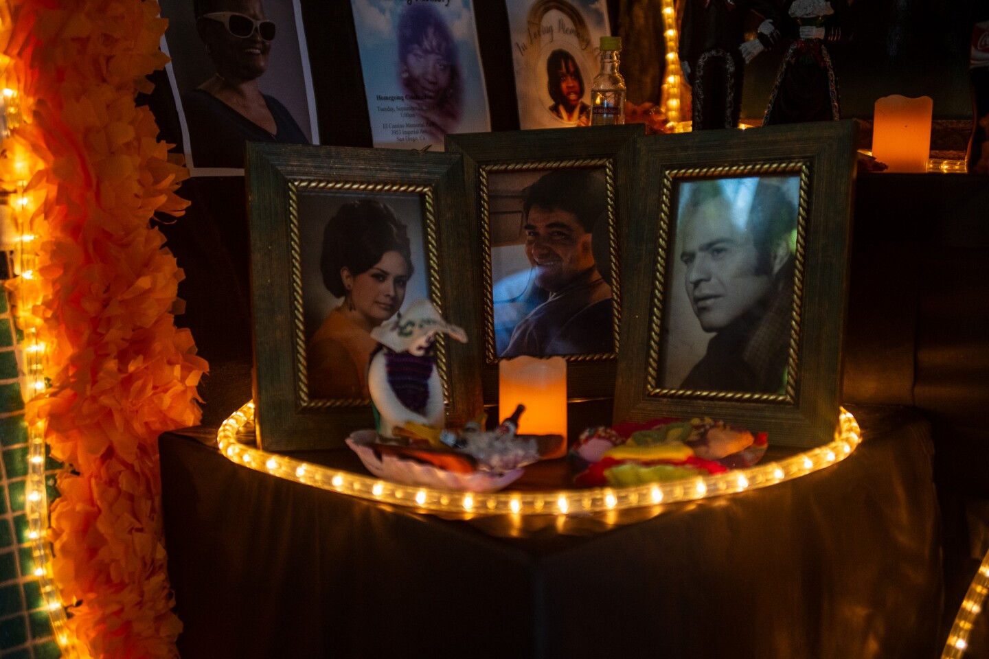 Photos of deceased loved ones sit on a table with rope lights illuminating their faces on an altar at the Sherman Heights Community Center in San Diego on Oct. 17, 2023.